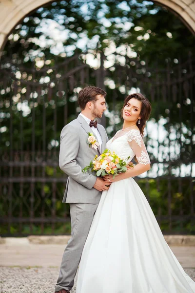 Beau marié câlin belle mariée avec bouquet dans romantique parc européen — Photo