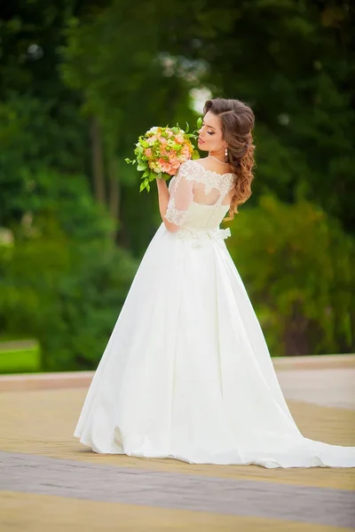 Noiva em um vestido branco longo com um buquê de pé — Fotografia de Stock