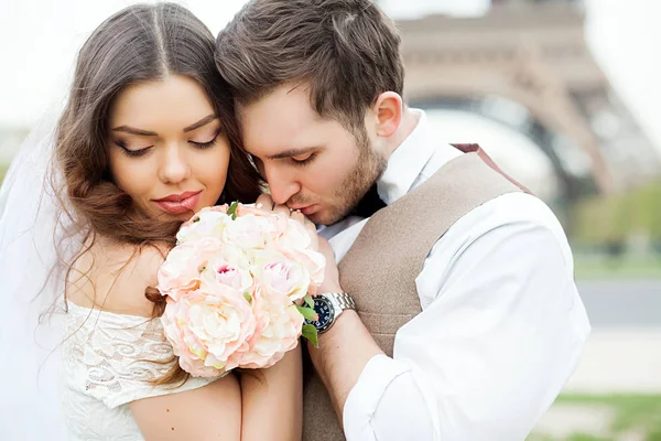 Sposo e sposo seduti su panchina nel parco, tenendosi per mano e bouquet. Sposo tenendo la testa sulla spalla della sposa e la sposa sorridente ampiamente . — Foto Stock
