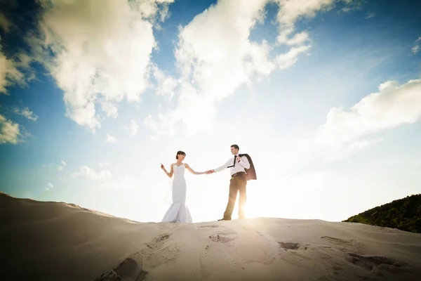 Sposa e sposo che si tengono per mano e corrono attraverso la sabbia sulla th — Foto Stock