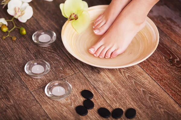 Manicured female feet in spa wooden bowl with flowers and water closeup