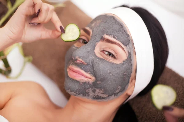 Mujer en un salón de belleza, bienestar. La cara de la mujer procedimiento cosmético en la máscara mitigación y rodajas de pepino en los ojos — Foto de Stock