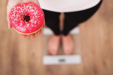 Diyet. Donut tutan ölçek ağırlığında üzerinde vücut ağırlığı ölçüm kadın. Tatlılar sağlıksız abur cubur var. Diyet, sağlıklı beslenme, yaşam tarzı. Kilo kaybı. Obezite. Üstten Görünüm