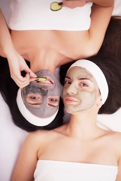 Retrato de dos hermosas chicas con crema facial en sus caras mirando a la cámara y tumbadas cara a cara en el suelo y sonriendo —  Fotos de Stock