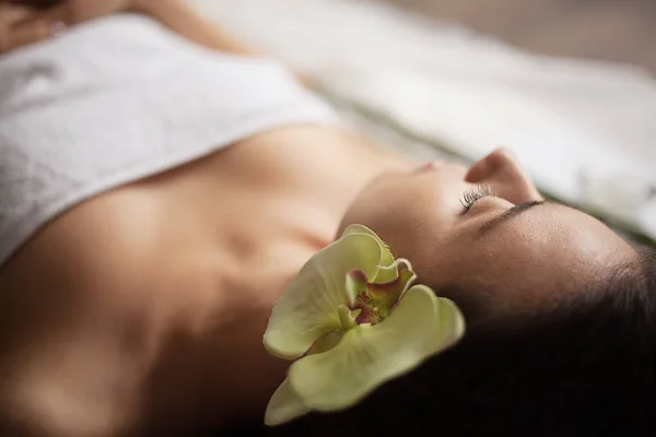 Hermosa chica en un salón de belleza con flor de orquídea en su cabello. tratamientos de spa. primer plano — Foto de Stock