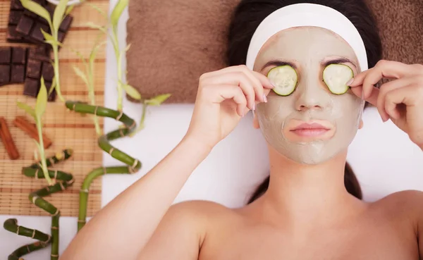 Hermosa mujer joven en máscara de barro de barro en la cara que cubre los ojos con rodajas de pepino . — Foto de Stock