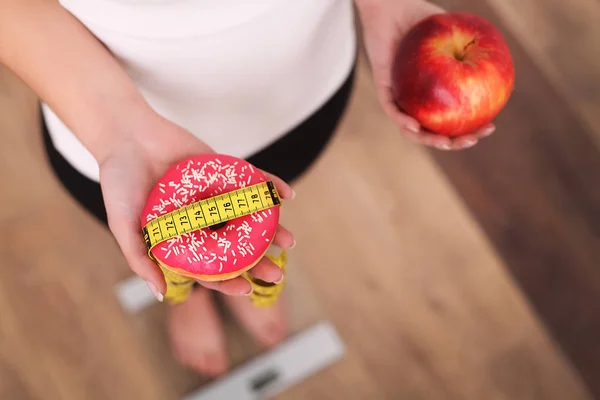 Diet. Woman Measuring Body Weight On Weighing Scale Holding Donut and apple. Sweets Are Unhealthy Junk Food. Dieting, Healthy Eating, Lifestyle. Weight Loss. Obesity. Top View