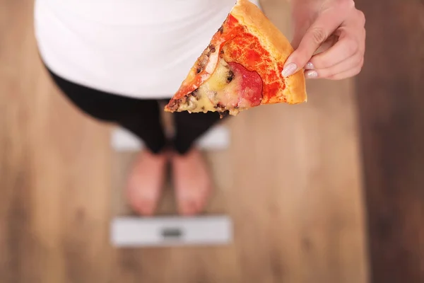 Диета. Женщина измеряет массу тела по взвешенной шкале, держа пиццу. Свитс вредная вредная пища. Диета, здоровое питание, стиль жизни. Потеря веса. Ожирение. Вид сверху — стоковое фото