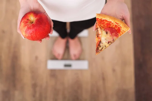 Régime alimentaire. Femme mesurant le poids corporel sur l'échelle de pesée tenant la pizza. Les bonbons sont malsains malbouffe. Régime alimentaire, saine alimentation, mode de vie. Perte de poids. Obésité. Vue du dessus — Photo