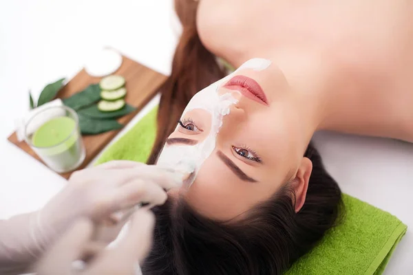 Young beautiful woman receiving clay facial mask in spa beauty salon. Skin care, Beauty treatments.