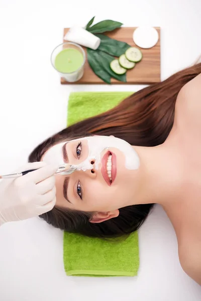 Cosmético aplicando mascarilla de belleza facial para mujer joven y hermosa en el salón de spa — Foto de Stock