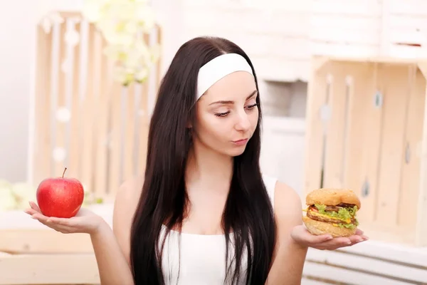 Молода жінка вирішує між гамбургером і яблуком. здоровий спосіб життя — стокове фото