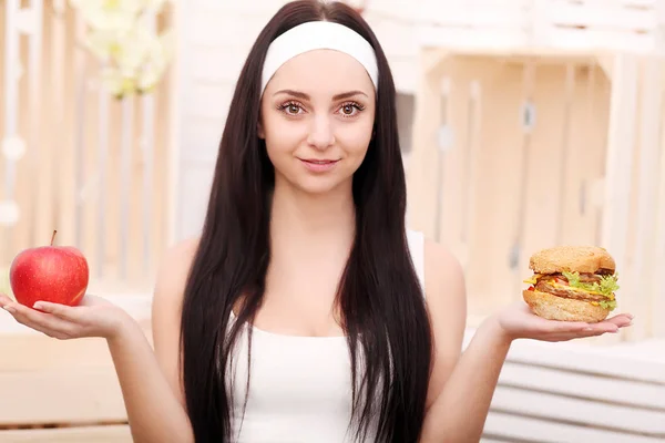 Eine junge Frau entscheidet sich zwischen Hamburger und Apfel. Gesundes Leben — Stockfoto