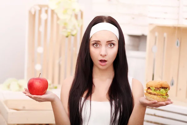 A young girl sits at home and makes a choice between healthy foo — Stock Photo, Image