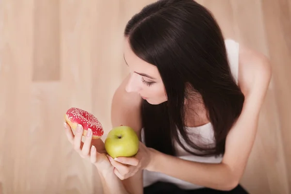 Estilo de vida saludable o concepto de nutrición con una mujer joven sosteniendo en las manos una manzana verde y un donut — Foto de Stock