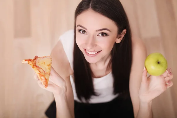 Estilo de vida saludable o concepto de nutrición con una mujer joven sosteniendo en las manos una manzana verde y una pizza —  Fotos de Stock