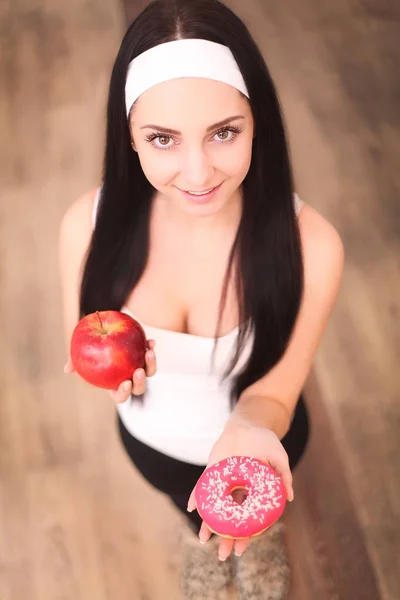 Belle jeune femme faisant le choix entre pomme et beignet sur fond de bois — Photo