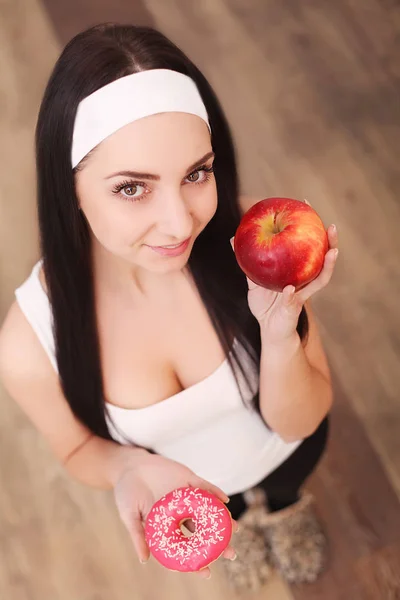 Schöne junge Frau macht die Wahl zwischen Apfel und Donut auf Holz Hintergrund — Stockfoto