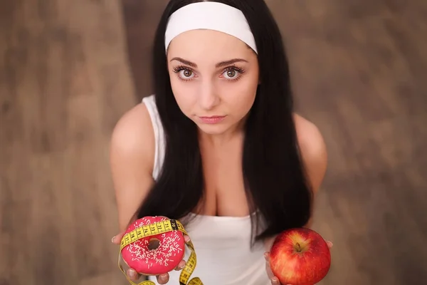 Beautiful young woman making choice between apple and donut on wood background — Stock Photo, Image