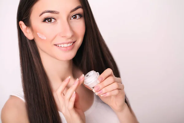 Bellezza, persone, cosmetici, cura della pelle e concetto di salute - felice sorridente giovane donna applicando crema al suo viso — Foto Stock