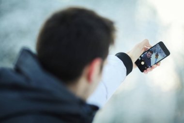 Genç bir adam fotoğrafı bir kış fotoğraf çekimi sırasında telefonda yapar. Selfies.