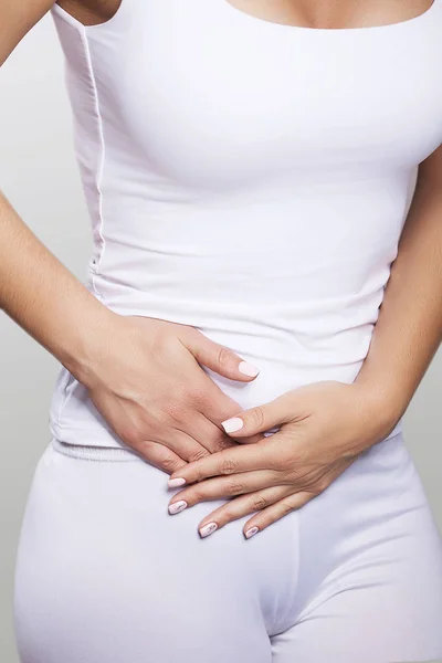 Stomach ache. Painful sensations on the right side of the abdomen. Appendicitis. Young woman holding hands on her stomach. The concept of health. On a gray background. Royalty Free Stock Photos