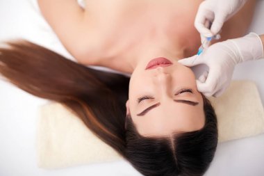 Neşeli genç kadın botox yordamı olmaya başladı. Doktor onun yanında duran ve gülümseyerek. O şırınga tutarak ve kadın yüzüne dokunmak