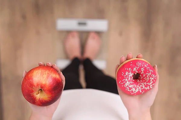 Vista de cerca de la mujer haciendo la elección entre la manzana y la dona con escamas borrosas en el fondo. Concepto de dieta —  Fotos de Stock