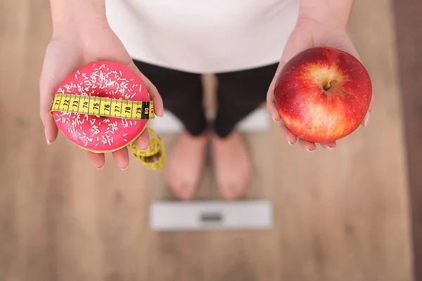 배경에 애플과 흐린된 비늘으로 도넛 사이 선택을 여자의 보기를 닫습니다. 다이어트 개념 — 스톡 사진