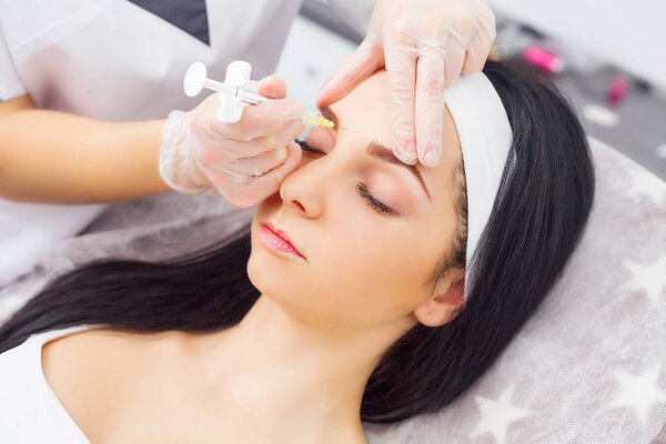 Close up of hands of cosmetologist making botox injection in female lips. She is holding syringe. The young beautiful woman is receiving procedure with enjoyment