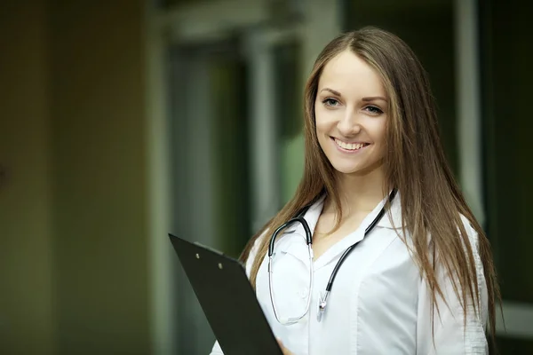 Medicine. A beautiful smile from a doctor in a woman's medical clothes. A young doctor. Graduate student. Family doctor is a woman. In a white dressing gown in the hospital. — Stock Photo, Image
