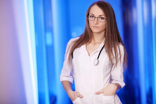 Medicine. Smiling young family doctor. On a blue background. On the neck is a stethoscope. In a white dressing gown. Graduate student. Young beautiful woman. Suction. — Stock Photo, Image