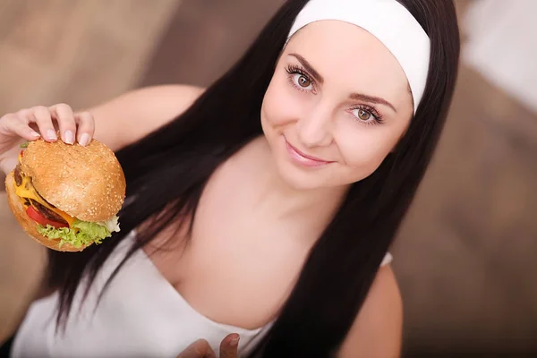 Manger malsain. Concept de malbouffe. Portrait de jeune femme à la mode tenant un hamburger et posant sur un fond de bois. Ferme là. Espace de copie. Cheveux, peau, maquillage et manucure parfaits. Plan studio — Photo