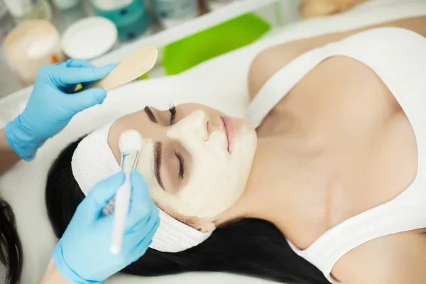 Woman lying on massage table in health spa while facial mask is — Stock Photo, Image