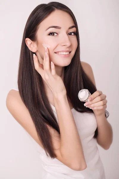 Applicare la crema cosmetica. Una bella giovane donna che applica crema idratante viso. Cura del viso e delle mani — Foto Stock