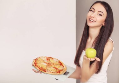 Diyet. Pizza ölçekler üzerinde tutan bir genç kadın. Sağlıklı beslenme kavramı
