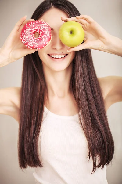 Dieta. Una mujer joven sosteniendo una pizza en la balanza y hacer una elección entre una manzana y un donut. El concepto de alimentación saludable —  Fotos de Stock
