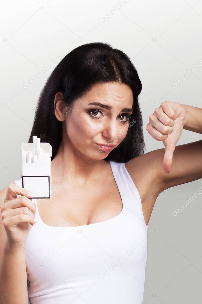 No smoking. Young beautiful woman agitating against smoking. Holds a packet in his hands despises smoking. The concept of health. On a gray background.