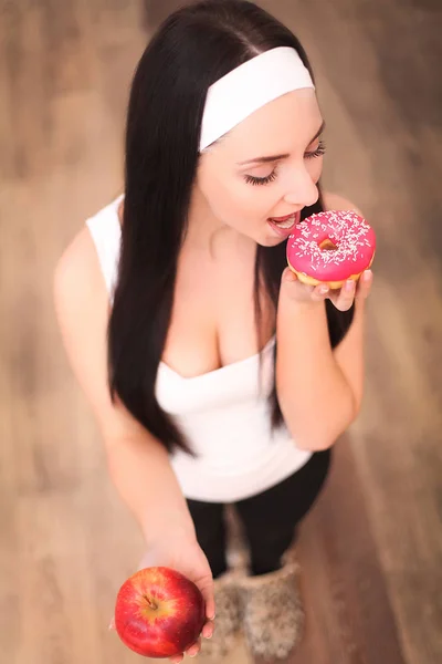 Hermosa joven mujer haciendo elección entre la manzana y el donut, de cerca —  Fotos de Stock