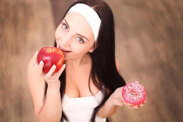 Beautiful young woman making choice between apple and donut, close up — Stock Photo, Image