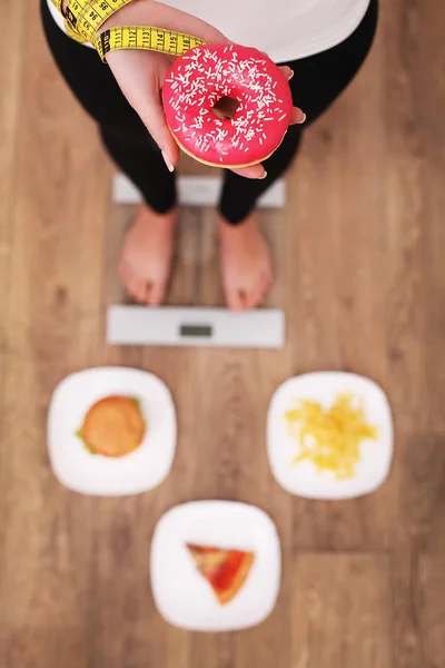 Giovane bella donna in piedi su scale e in possesso di una ciambella. Il concetto di alimentazione sana. Stile di vita sano. Dieta . — Foto Stock