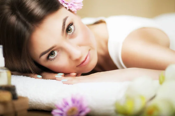 Porträt eines schönen Mädchens in einem Wellnessbereich. Sanfter Blick. Blumen im Haar. Aromaöl. Massageschrank. das Konzept der Gesundheit und Schönheit. — Stockfoto