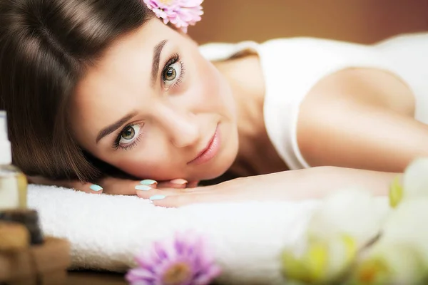 Masaje. Hermosa mujer en el spa. Mirada gentil. Flores en el pelo. El concepto de salud y belleza. Fondo oscuro. Salón de spa . —  Fotos de Stock