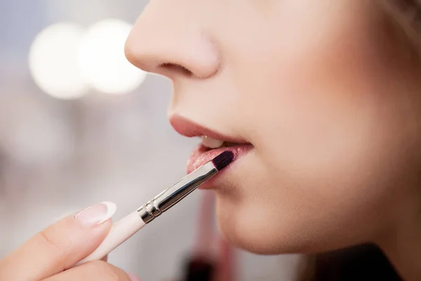 Visagistin trägt Lippenstift mit Pinsel auf Modellippen auf — Stockfoto