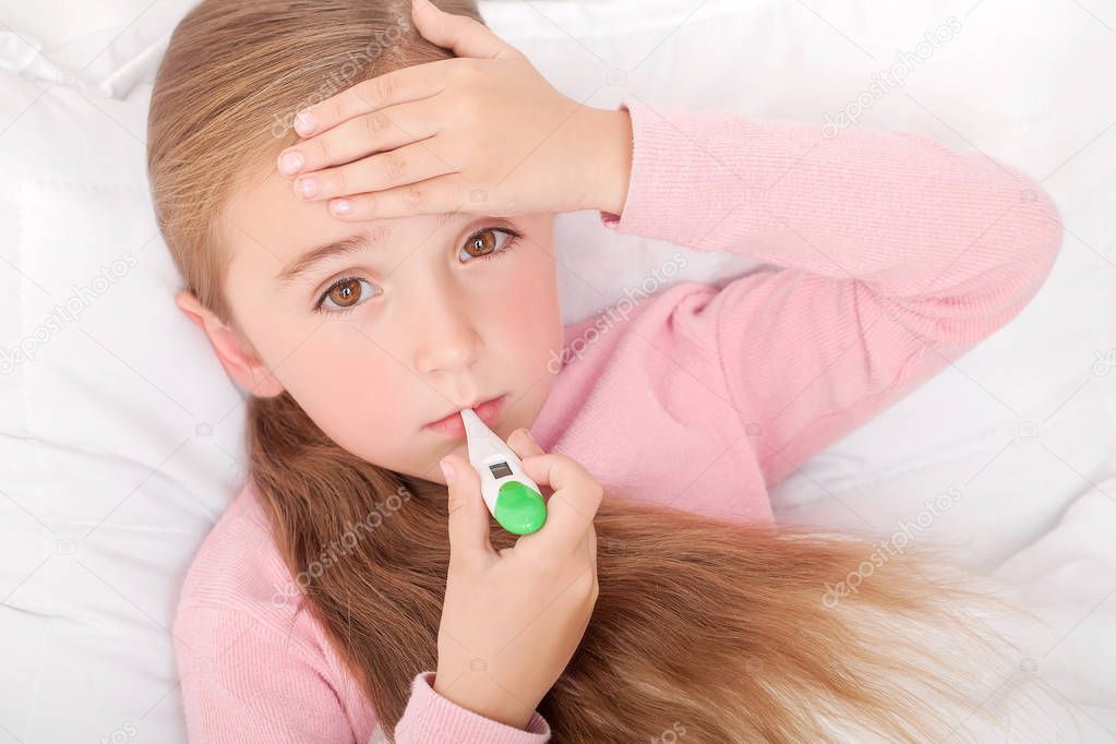 Sick girl lying in bed with a thermometer in mouth