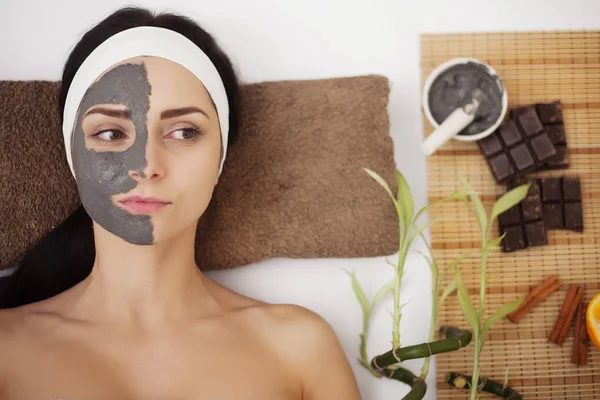 Masaje spa para mujer joven con mascarilla facial en la cara - en interiores — Foto de Stock