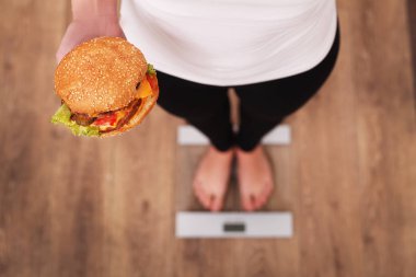 Diyet. Kadın ölçme vücut ağırlığı üzerinde ağırlığında ölçek Holding Burger ve elma. Tatlılar sağlıksız abur cubur var. Diyet, sağlıklı beslenme, yaşam tarzı. Kilo kaybı. Obezite. Üstten Görünüm