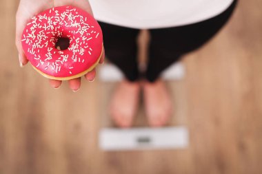 Diyet. Donut tutan ölçek ağırlığında üzerinde vücut ağırlığı ölçüm kadın. Tatlılar sağlıksız abur cubur var. Diyet, sağlıklı beslenme, yaşam tarzı. Kilo kaybı. Obezite. Üstten Görünüm