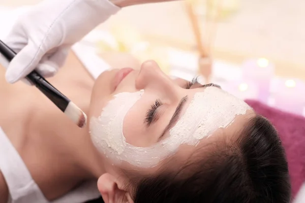 Mooie jonge vrouw krijgt facial klei masker in spa, liggend — Stockfoto