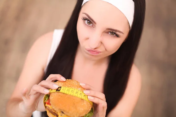 Eine junge Frau hält einen Burger in einem Maßband. steht ein Mädchen auf einem hölzernen Hintergrund. die Aussicht von oben. das Konzept der gesunden Ernährung. — Stockfoto